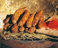 Salsicce pezzenti dal tipico colore rosso ruggine con macchie bianco-gialle delle parti grasse; i pezzi sono impilati gli uni sugli altri; sfondo rustico