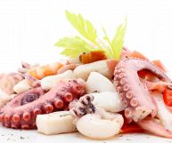 Gamberi, moscardini, seppie e polpo sono gli ingredienti di una saporita insalata di frutti di mare su cui è poggiata una foglia di sedano; sfondo bianco