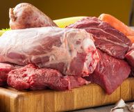 Sopra uno spesso tagliere in legno chiaro sono alcuni pezzi di carne di mucca ancora d cuocere, dal colore rosso intenso con parti adipose più o meno presenti
