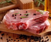 Su un tagliere rettangolare in legno, due spesse fette di carne suina ancora da cuocere, dalla carne tenera e parti lipidiche visibili