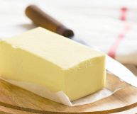 Un panetto di margarina su carta oleata; sotto un tagliere rotondo, dietro un coltello sfocato con un manico di legno marrone scuro