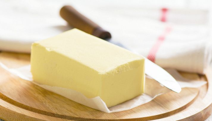 Un panetto di margarina su carta oleata; sotto un tagliere rotondo, dietro un coltello sfocato con un manico di legno marrone scuro