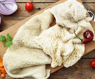 Trippa sbiancata su un tagliere circondato da cipolla viola tagliata a metà, carote a rondelle, pomodori ciliegini, peperoncino fresco e prezzemolo