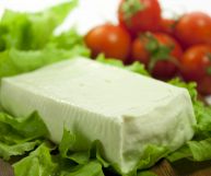 Uno stracchino fresco, dalla pasta cremosa di colore bianco latte; sotto, un letto di lattuga; dietro, sfocati, pomodori rotondi di un bel rosso brillante