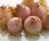 Lampascioni sott'olio con origano su un piatto bianco; la forma è a metà tra una cipolla e l’aglio; la superficie è lucida, con sfumature rosate tendenti al viola
