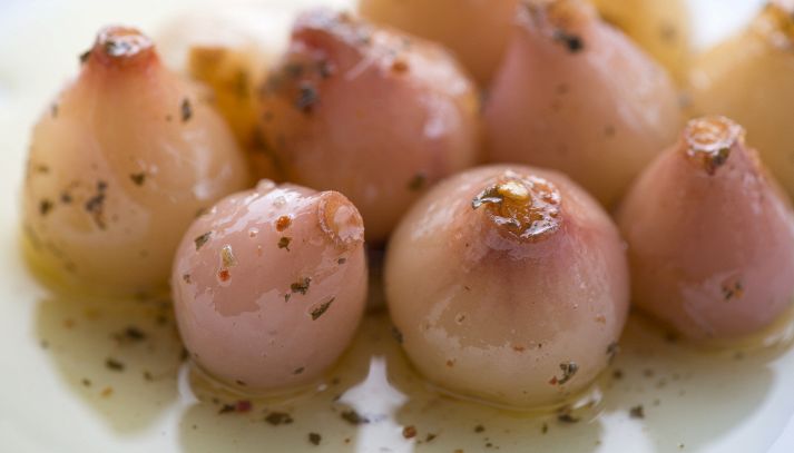 Lampascioni sott'olio con origano su un piatto bianco; la forma è a metà tra una cipolla e l’aglio; la superficie è lucida, con sfumature rosate tendenti al viola