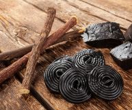 Su un tavolo di legno, tre radici di liquirizia in alto a sx, due blocchi di prodotto puro in alto a dx, cinque rotelle haribo in centro in basso