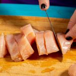 Tagliere con petto di pollo crudo che viene tagliato
