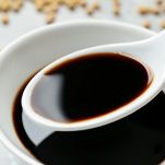 Spoon with soy sauce over bowl, closeup