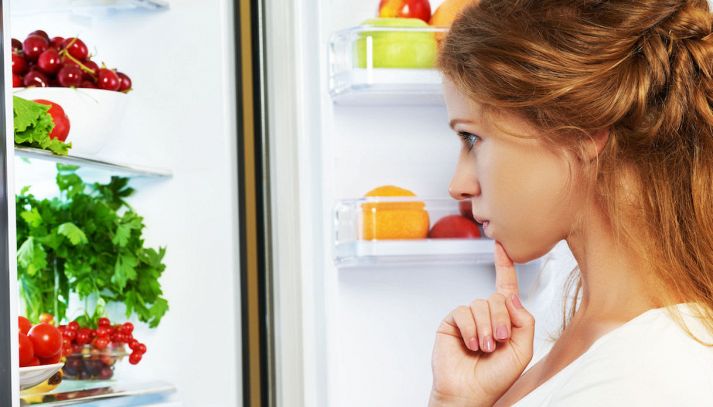 Donna che guarda frigo pieno di verdure