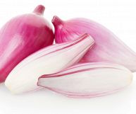 In primo piano una cipolla rossa di Tropea tagliata a metà, dietro due pezzi interi; la forma è ovoidale e allungata, il colore va dal bianco al violaceo