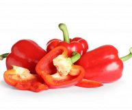 Isolati su sfondo bianco, peperoni rossi dalla consistenza soda e la pelle tesa e lucida; alcuni sono interi e altri a fette, con gambo verde chiaro