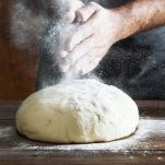 Man preparing bread dough on wooden table in a bakery close up