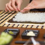 Hands of woman chef filling japanese sushi rolls with rice