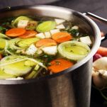 Broth with carrots, onions various fresh vegetables in a pot &#8211; colorful fresh clear spring soup. Rural kitchen scenery vegetarian bouillon