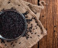 Sulla sinistra una scodella trasparente con riso nero Venere crudo, dai chicchi color ebano; la ciotola è su un pezzo di iuta su cui vi sono altri chicchi