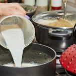 Mano versa il latte nel pentolino per la crema