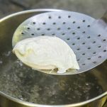 Cooking poached eggs. The egg is pulled out of the water with a