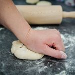 Close up on hand of unknown caucasian woman female girl making bread or pastry knead the dough kneading on the kitchen table at home side view