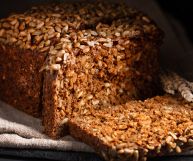 Pane nero di segale con mix di semi, poco lievitato e dal forte potere saziante; il bauletto è posato su uno strofinaccio chiaro su cui sono tagliate due fette