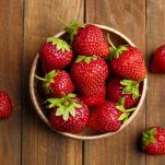 Delicious ripe strawberries in bowl on wooden table, flat lay