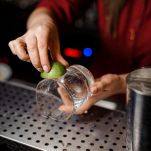 Female barman hands rubbing a glass with lime juice