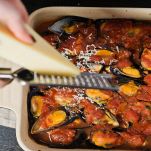 Donna grattugia pecorino sulla tiella di patate riso e cozze