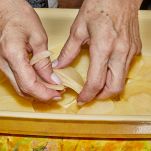 Donna mette uno strato di patate nella teglia in terracotta