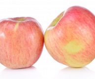Su sfondo bianco, due mele fuji dalla consistenza soda e la buccia intatta, dio colore rosso-rosato con striature ora gialle paglierino, ora arancioni chiaro