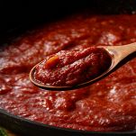 Raccogliere salsa di pomodoro nella padella con cucchiaio di legno