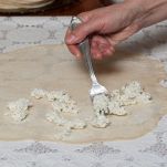 Donna distribuisce il formaggio sull’impasto della focaccia