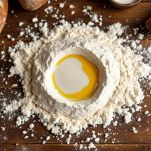 Farina a fontana con lievito e olio versati al centro in una ciotola di ceramica.