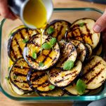 In un contenitore, alternate strati di melanzane grigliate con olio d'oliva