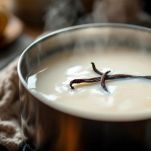 Un pentolino d'acciaio sul fuoco con latte bianco e una mezza stecca di vaniglia incisa in infusione.