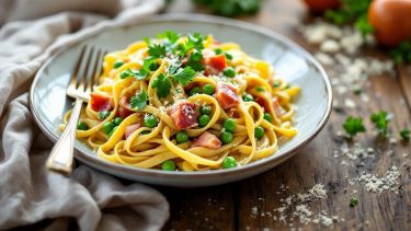 Piatto di tagliatelle con piselli e prosciutto servito caldo.