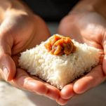 Mani che modellano onigiri triangolari con ripieno di tonno.