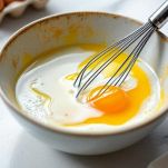 Ciotola con uovo, latte e olio mescolati con una frusta.