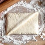 Mani che piegano impasto di pane su piano infarinato.