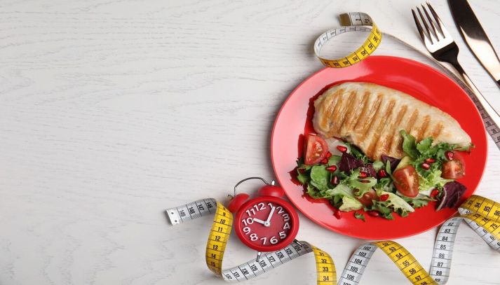 piatto con cibo e sveglia su un tavolo di legno bianco