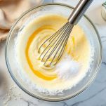 Uova sbattute con zucchero e latte in ciotola.