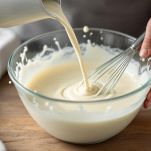 Latte vegetale versato in ciotola con farina e frusta.