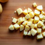 Patate tagliate a cubetti su tagliere di legno.