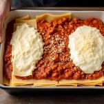 Pirofila con strati di lasagna, ragù e besciamella pronti per la cottura.