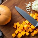 Cubetti di zucca e cipolla tritata su tagliere.