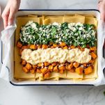 Pirofila con strati di lasagna, zucca e spinaci pronti per la cottura.