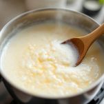 Pentolino con latte in ebollizione mescolato con cucchiaio di legno.