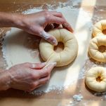 Mani che formano ciambelle di impasto su piano infarinato.