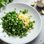 Trito di prezzemolo, aglio, cipollotto e peperoncino su tagliere.