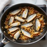 Sarde che cuociono in tegame con cipolla e olio.