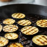 Fette di melanzane grigliate su piastra con segni di cottura.